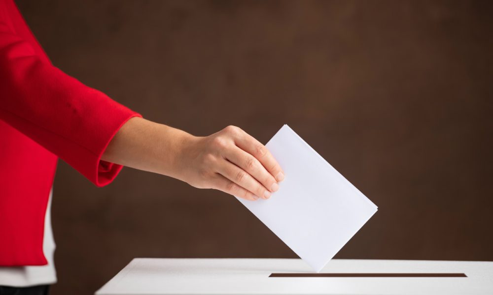 Woman hand throws voting ballot paper in ballot box, concept of a person voting during elections